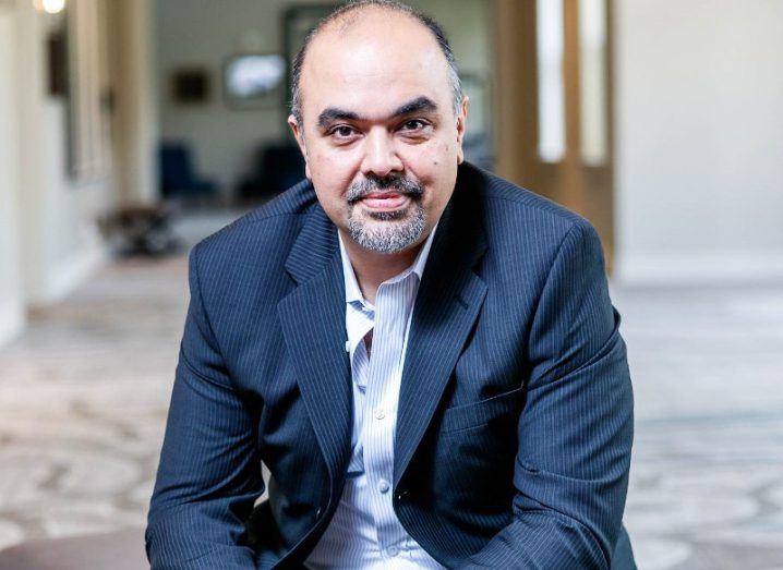 A man in a business suit sitting down, smiling at the camera.