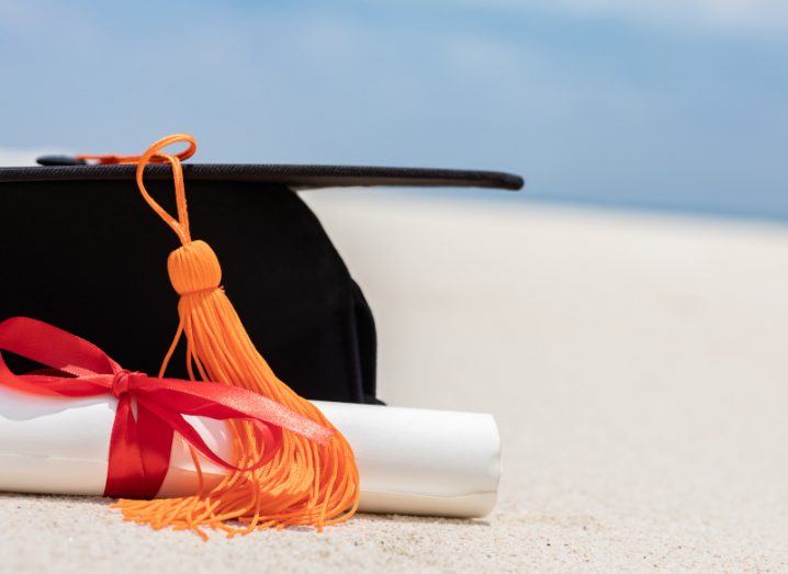 Close up of graduation hat and scroll on sand in a beach with the sea in the background.