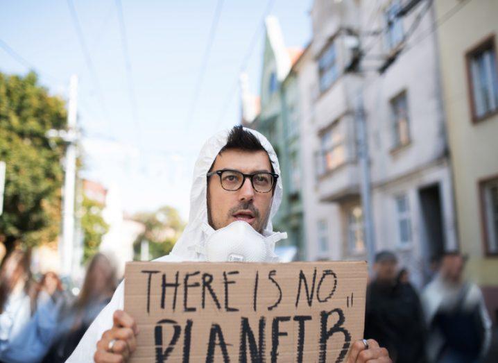 Man in white hoodie holding a placard that reads "There is no planet B" in a public demonstration.