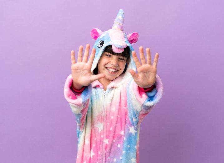 Child wearing unicorn costume with hands outstretched showing the number ten.