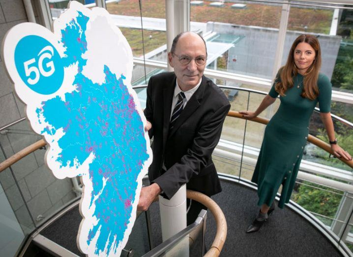 A man standing in a stairwell with a woman behind him holding up a huge cardboard cutout of Ireland showing where 5G is available.