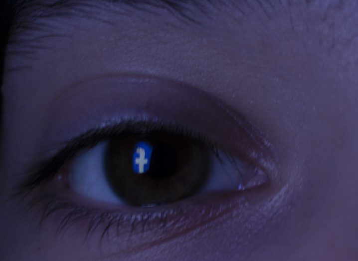Inverted Facebook logo reflected in a person's eye.