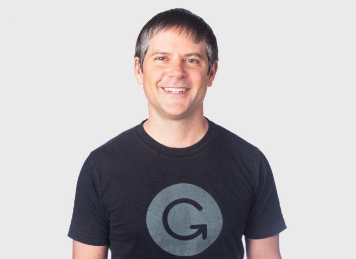 A person is smiling at the camera, wearing a blue T-shirt that has the Grammarly logo on it.