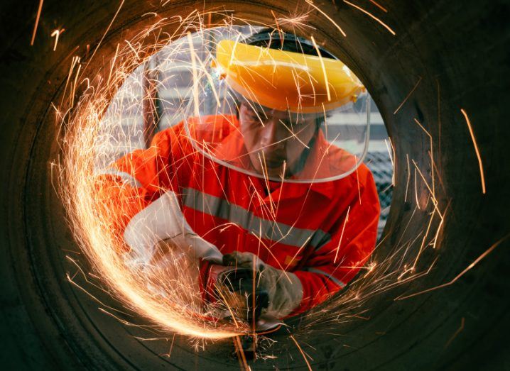 Uniformed factory worker uses a grinder on a metallic structure with sparks flying.