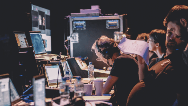 Ann O'Dea sits backstage with the AV team at Inspirefest, surrounded by monitors and production equipment, intently watching what's happening live onstage.