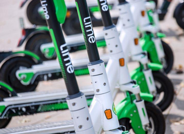 Lime e-scooters with company branding parked in a row. The bikes are black, green, and white in colour.