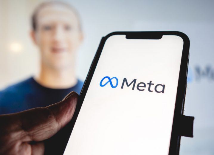 Meta logo on a smartphone screen with Mark Zuckerberg's blurred picture in the background.