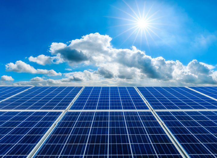 Solar panels under a blue sky with clouds and a shining sun.