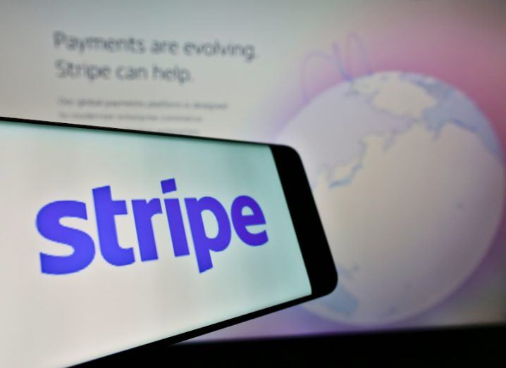 Stripe logo on a smartphone screen. A blurred website on a laptop screen in the background reads "Payments are evolving. Stripe can help".