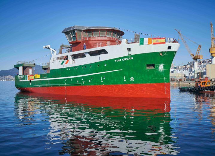 The RV Tom Crean docked at Vigo, Spain. It is coloured green, red and white, with the Irish and Spanish flags hanging from the front.