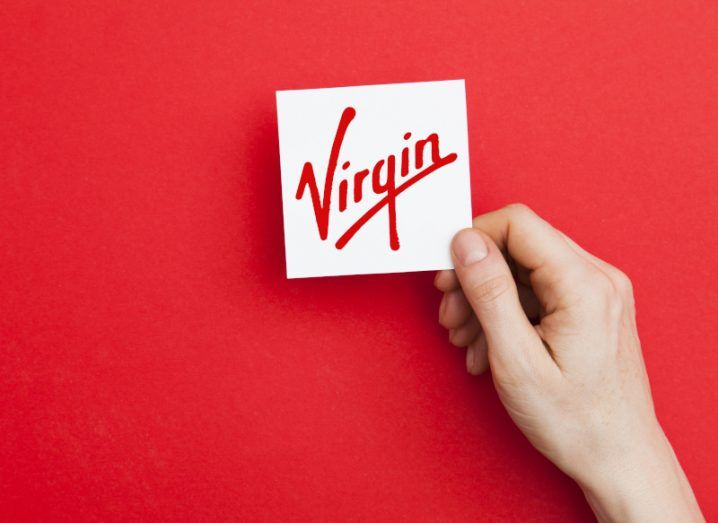 Virgin logo on a card held by hand in a red background.