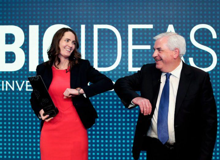 Xtremedy co-founder Dr Lyn Markey and Enterprise Ireland executive director Stephen Creaner standing on a stage and touching their elbows against each other to replace a handshake. Big Ideas branding is in the background.