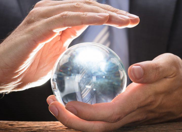 Crystal ball held in one hand as another hovers over it. The person holding the ball is wearing a business suit.