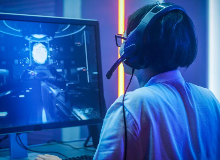 Person wearing a headset while playing a game on a computer, with a monitor in front of them.