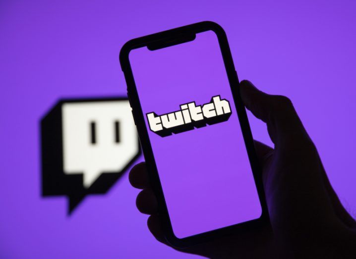 A person holds up a phone with the Twitch logo on the screen.