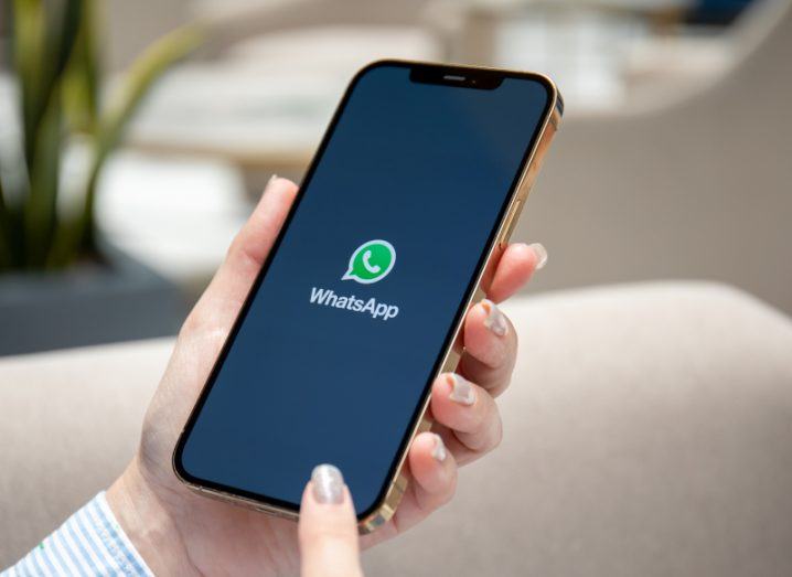 A phone with a WhatsApp logo on the screen being held by a woman's hand.
