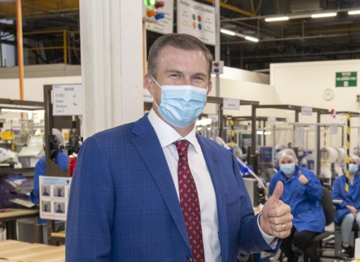 Medtronic CEO Geoff Martha in a mask giving a thumbs up to the camera, with a masked employee behind him.