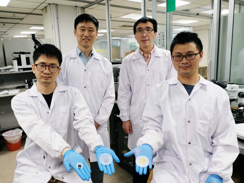 Four men stand in a lab wearing lab coats. Two of the men are holding paper-thin batteries in their gloved hands.