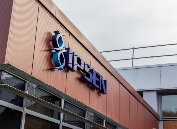 Ipsen logo in blue letters on the front of a building with brown panels and sky in the background.