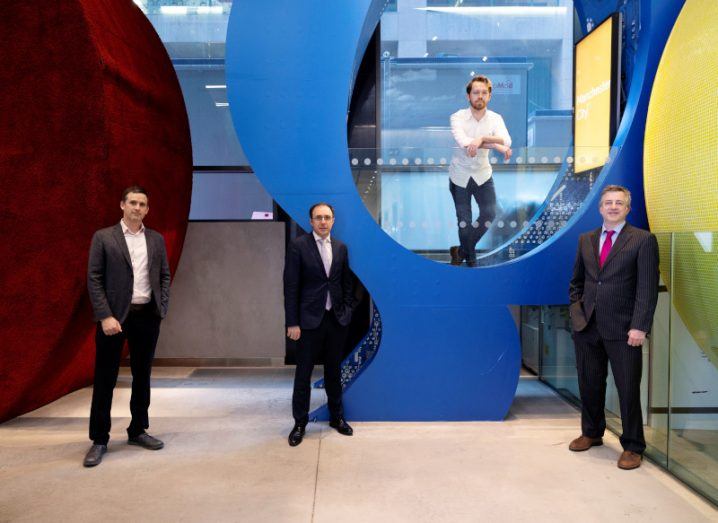 Four men stand in a colourful office space.