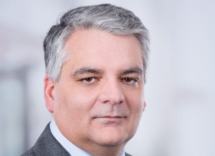 Headshot of Mel Chittock looking at the camera with a grey background behind him.