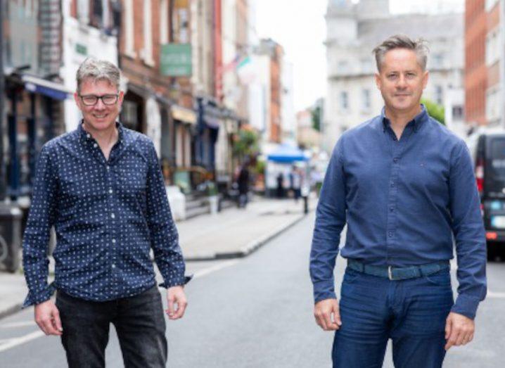 Two men in shirts in blue shirts and jeans stand on a street in Dublin where Strikepay is helping customers with its payments technology.