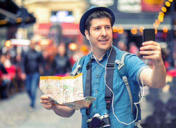 Male tourist taking a selfie in a crowded European city and using his phone with roaming.