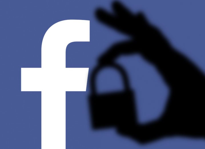 Silhouette of hand holding a lock with Facebook logo in the background.