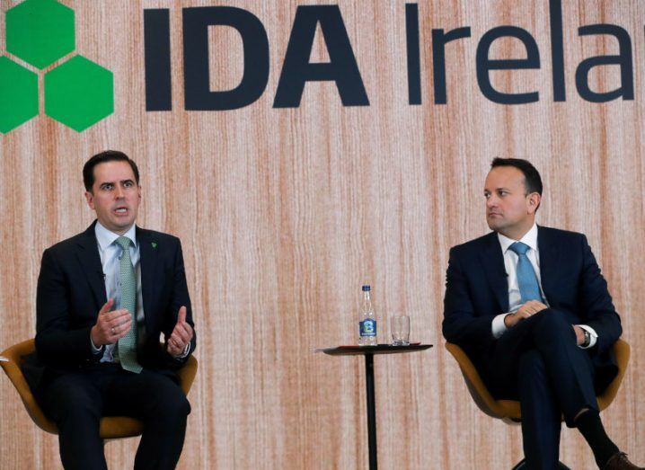 IDA CEO Martin Shanahan and Tánaiste Leo Varadkar seated on a stage with Shanahan talking while Varadkar stares at him. The IDA Ireland logo can be seen on a wall in the background.