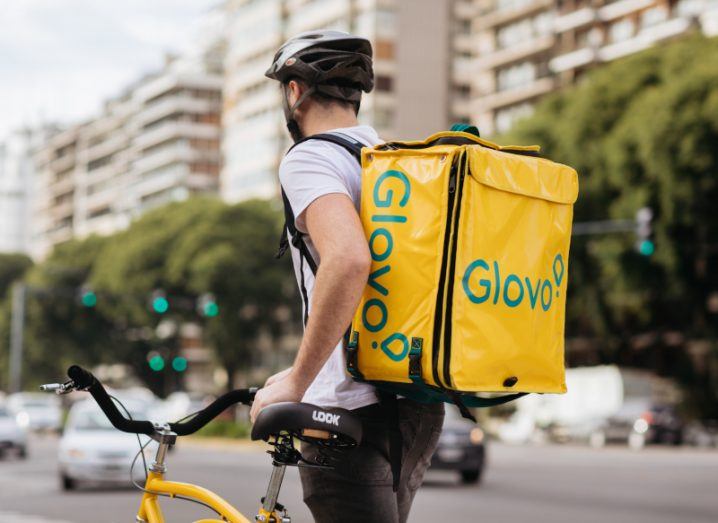 Glovo delivery driver standing next to a bike on a city street.