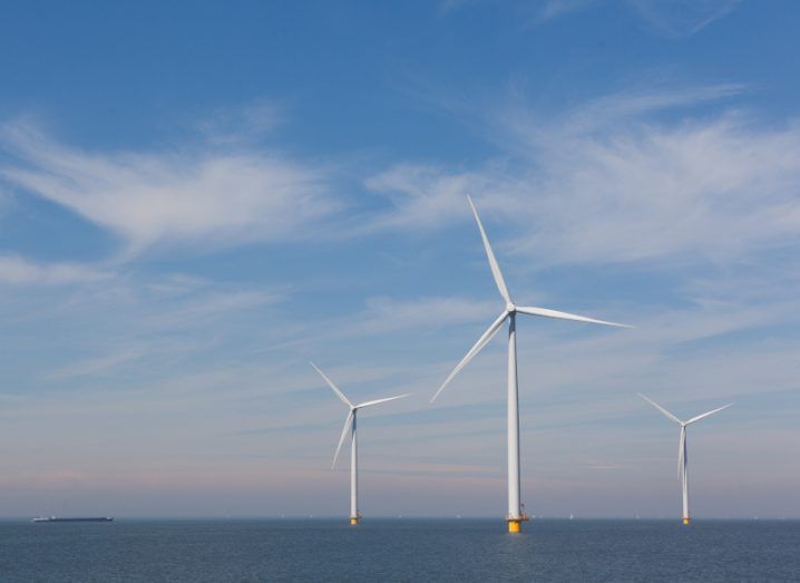 Three large offshore wind turbines sit in the sea beneath a cloudy blue sky.