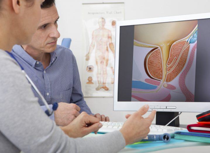 A doctor consults with a patient, explaining his condition using a diagram of the prostate gland on his computer screen.