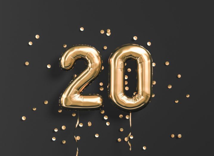 Gold foil balloons shaped like the number 20 surrounded by gold confetti on a charcoal background.
