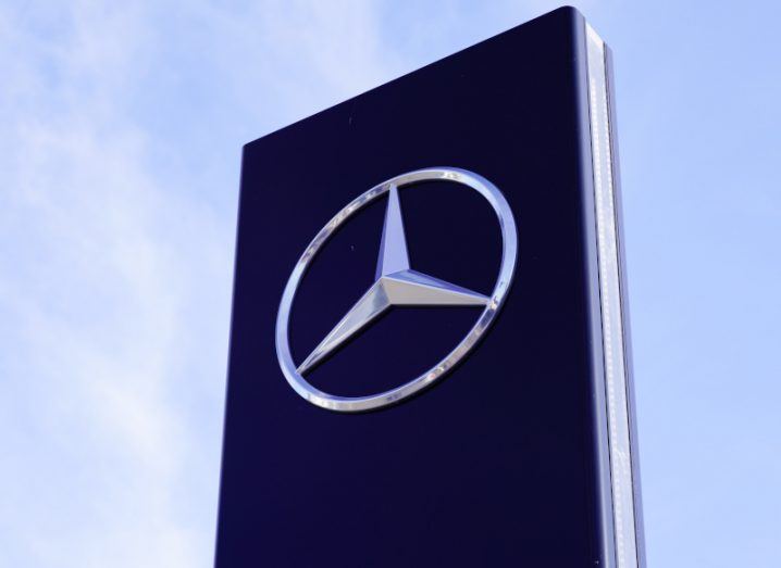 The logo of Mercedez-Benz on a dark blue sign with a blue sky in the background.