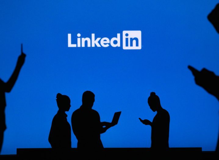 Workers silhouetted in black standing with their phones against a blue background with the LInkedIn logo on it.