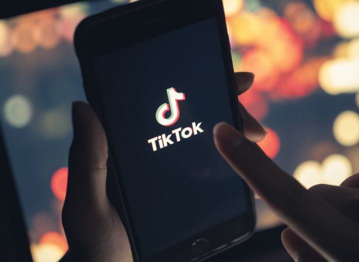 A person is holding a phone with the TikTok logo on the screen.