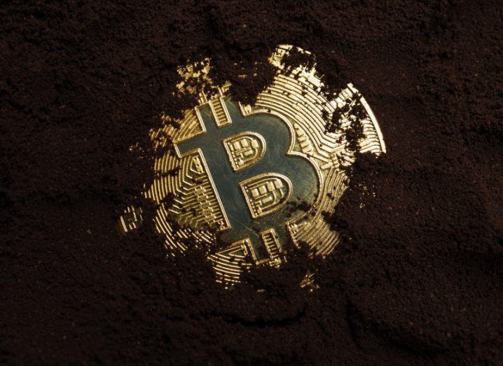 A golden bitcoin covered in soil.
