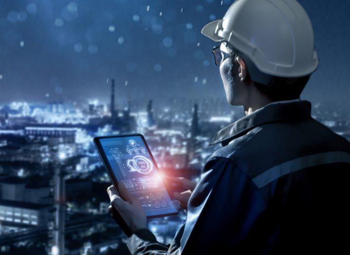 Engineer holding a tablet device with a lit up city in the background.