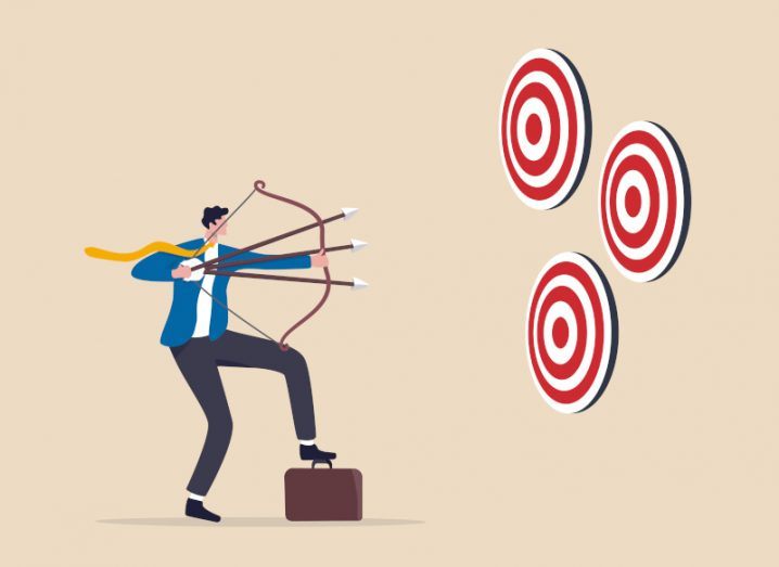 Businessman using bow and arrow to aim three arrows simultaneously at three different targets.