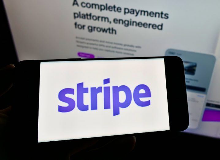 Stripe logo on a mobile phone with the company's website on a screen in the background.