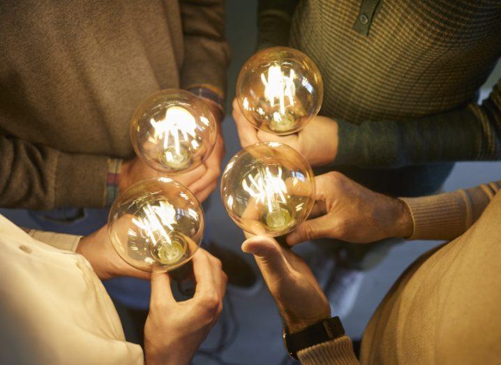 Four people stand in a circle, each holding a bright lightbulb.