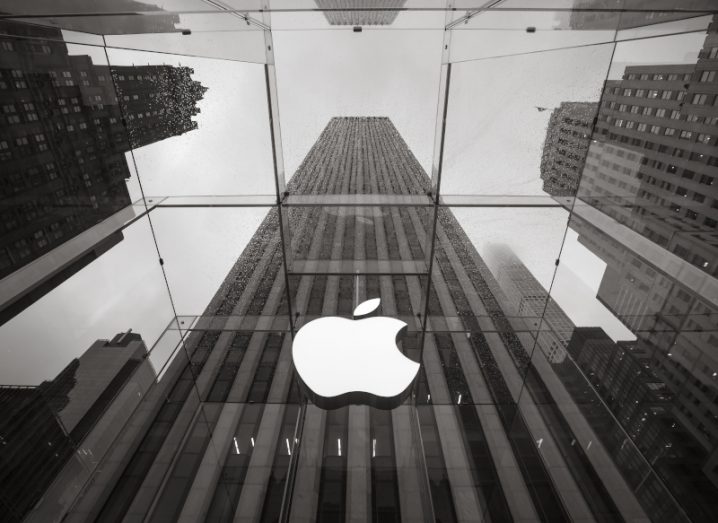 Black and white photo of Apple logo on its store in New York. Tall buildings and sky above.