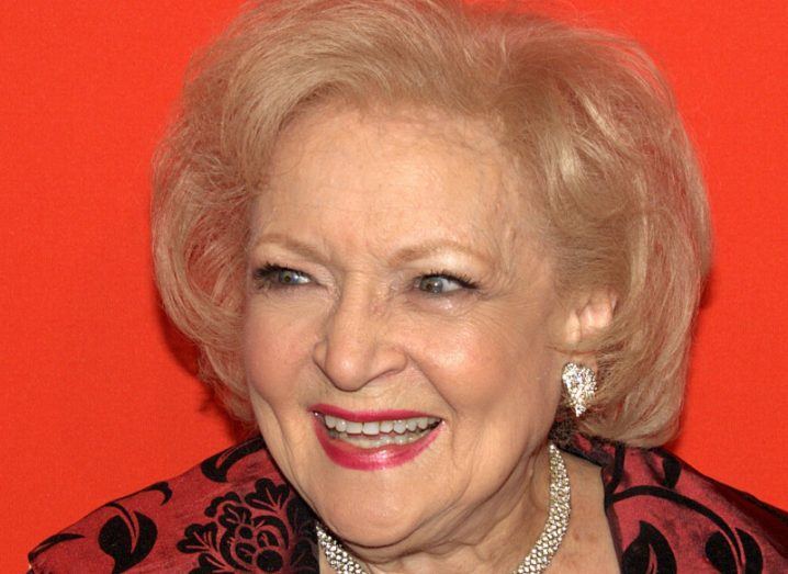 Headshot of Betty White smiling against a red background.