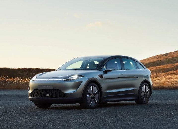 A steel grey SUV-type electric car standing on a road with hills in the background.