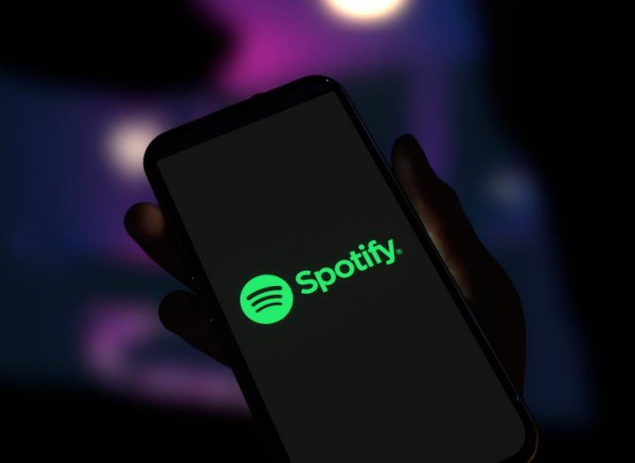 Spotify logo on a smartphone screen held in a person's hands.