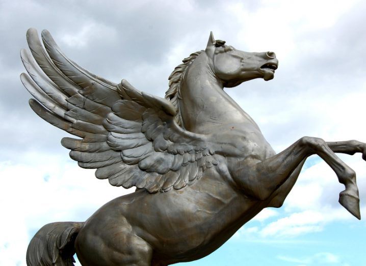 A grey pegasus statue with clouds and a blue sky in the background.