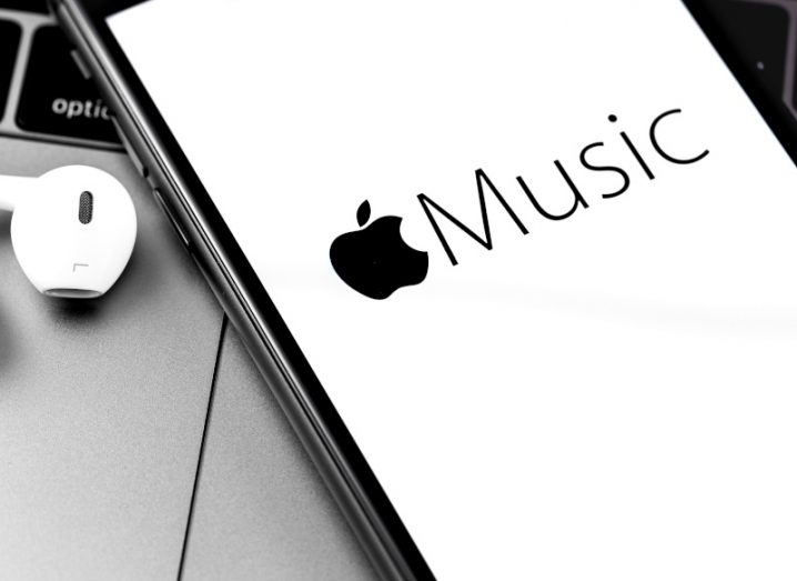 Apple Music logo on the white background of a mobile phone screen, placed on a laptop with an earphone next to it.