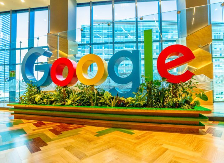 Google logo with plants under it, placed in the lobby of a building.