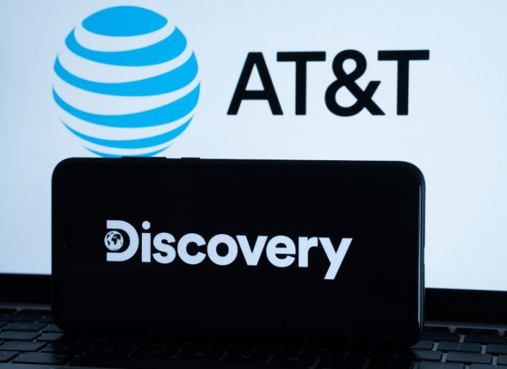 AT&T logo on a screen behind a Discovery logo on a black mobile phone screen.