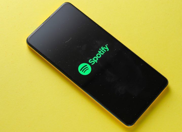 Spotify logo on the screen of a mobile phone on a yellow background.